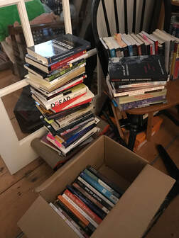Stacks of mostly philosophy books, on a chair, in a box, and on the floor. 
